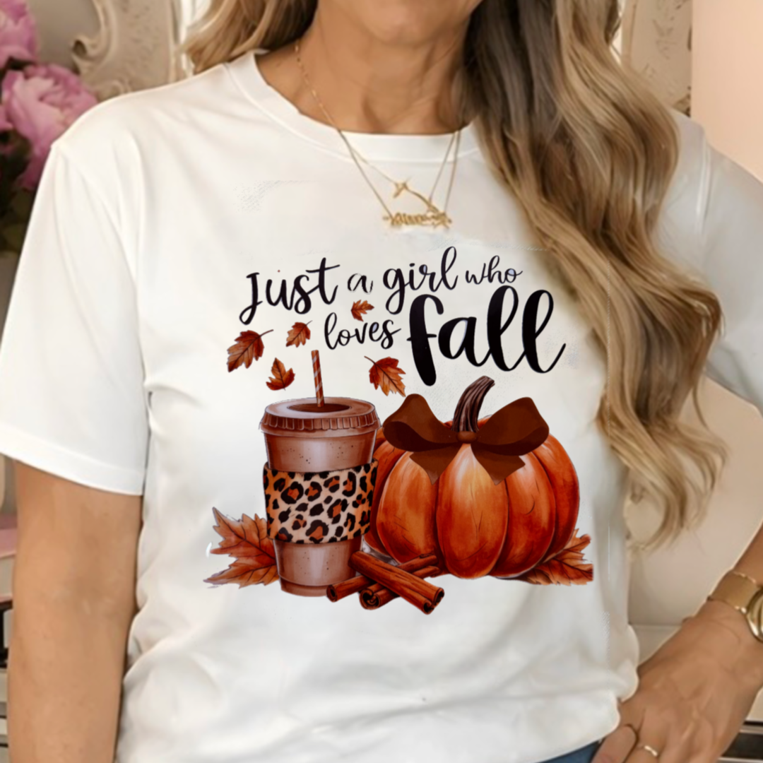 a white graphic t-shirt with a fall-themed design that reads 'Just a girl who loves fall' above pumpkins, leaves, cinnamon sticks, and a coffee cup.