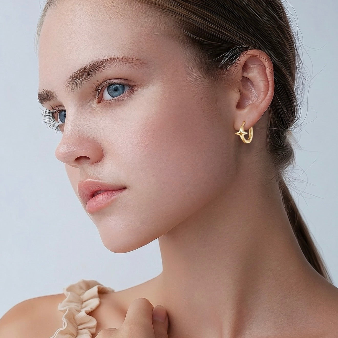 Close-up of a woman wearing a gold earring against a plain background