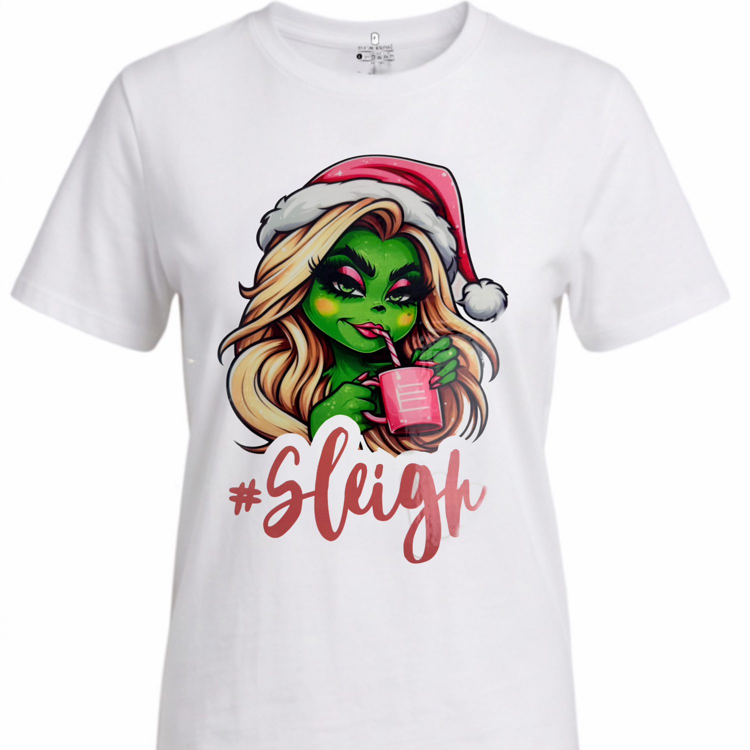 A white short-sleeve crewneck t-shirt featuring a cartoon graphic of a green-skinned woman with blonde hair wearing a red Santa hat and holding a pink drink, with the word '#Sleigh' written below in red script.