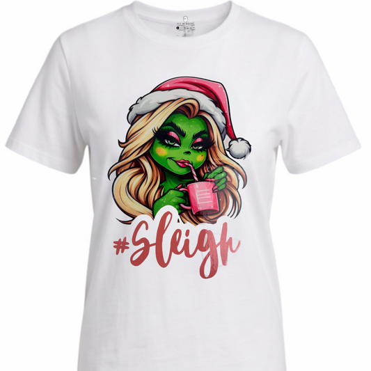 A white short-sleeve crewneck t-shirt featuring a cartoon graphic of a green-skinned woman with blonde hair wearing a red Santa hat and holding a pink drink, with the word '#Sleigh' written below in red script.