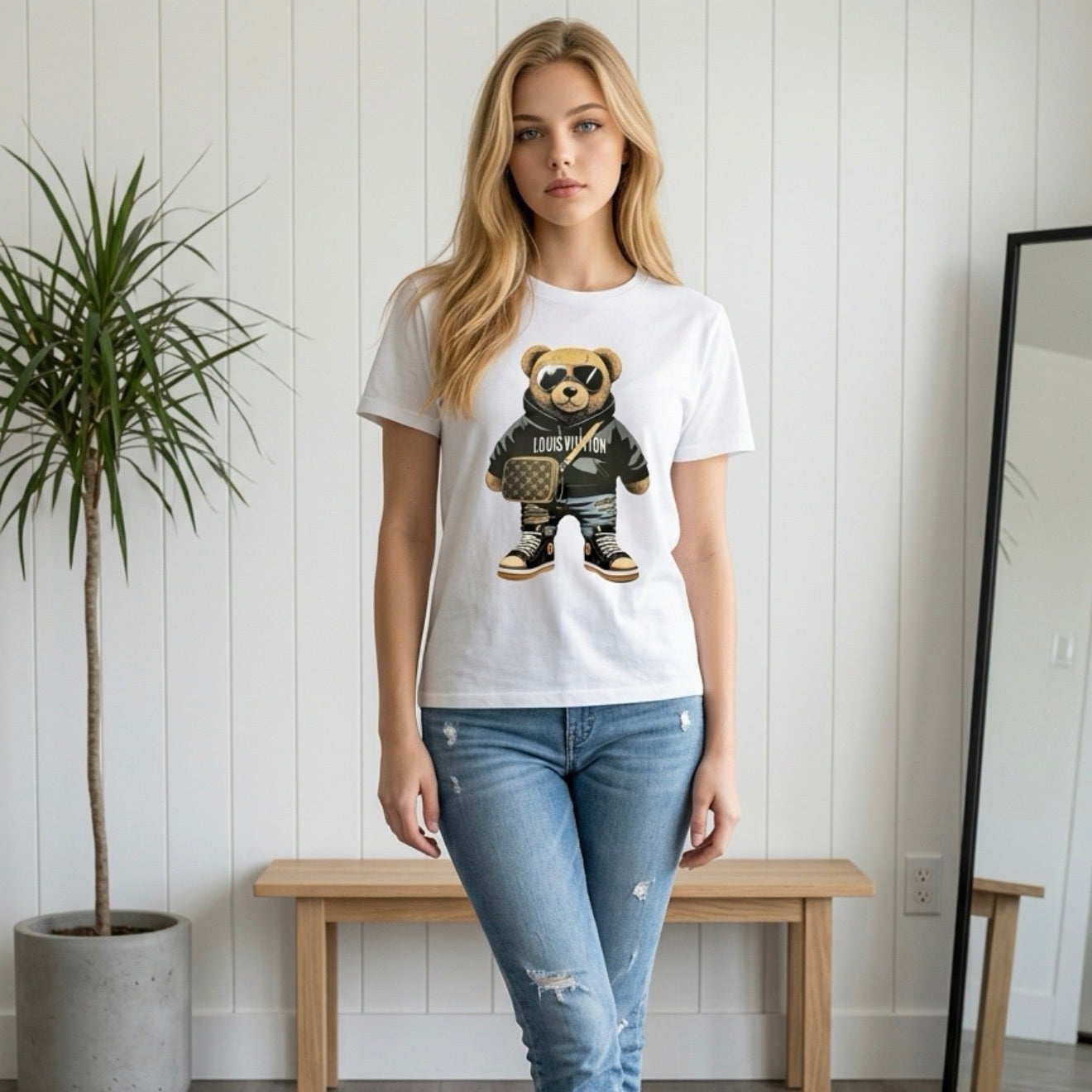 Person wearing a white t-shirt with a graphic design of a bear in a sweater, standing in a room with a wooden floor and white walls.