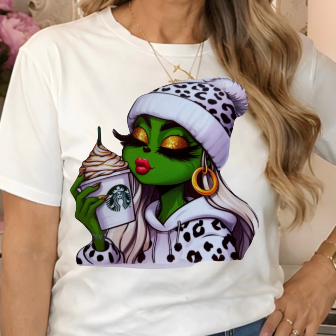 a white graphic t-shirt with a Glitzy Grinchette  character holding a Starbucks cup.