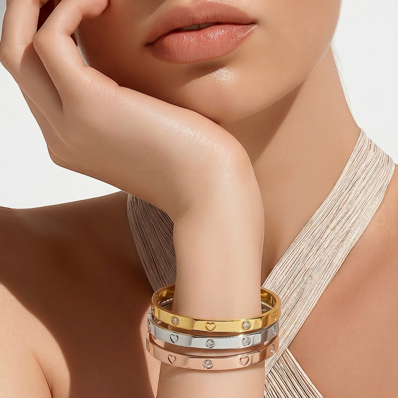 Close-up of a woman's arm wearing multiple gold bracelets on a neutral background