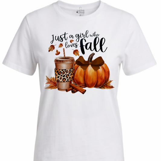 A white short-sleeve crewneck t-shirt featuring a fall-themed graphic print with the text 'Just a girl who loves fall' above a cup with leopard print, a pumpkin, leaves, and cinnamon sticks.