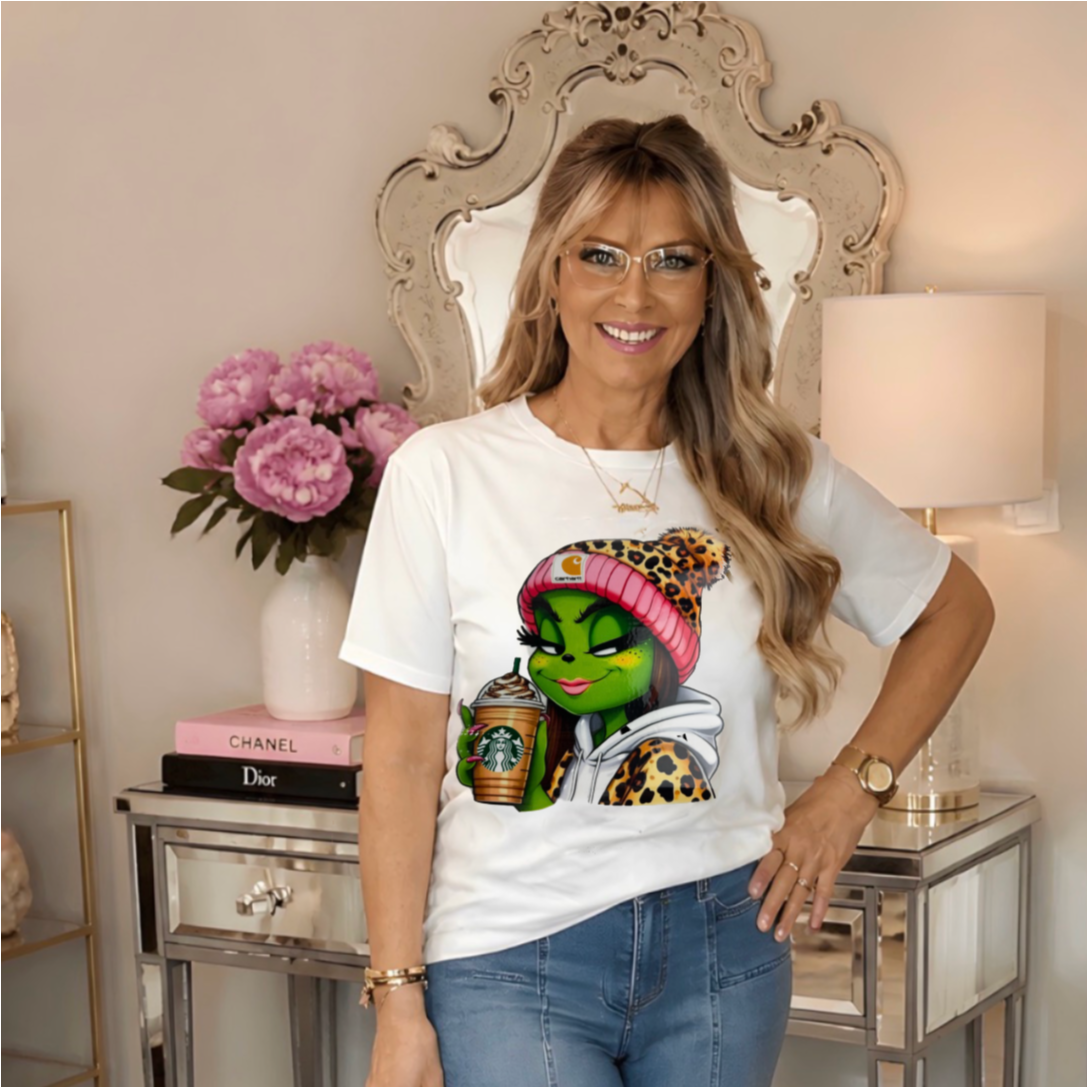 a white graphic t-shirt featuring a Grinchette character with a pink hat and leopard print.
