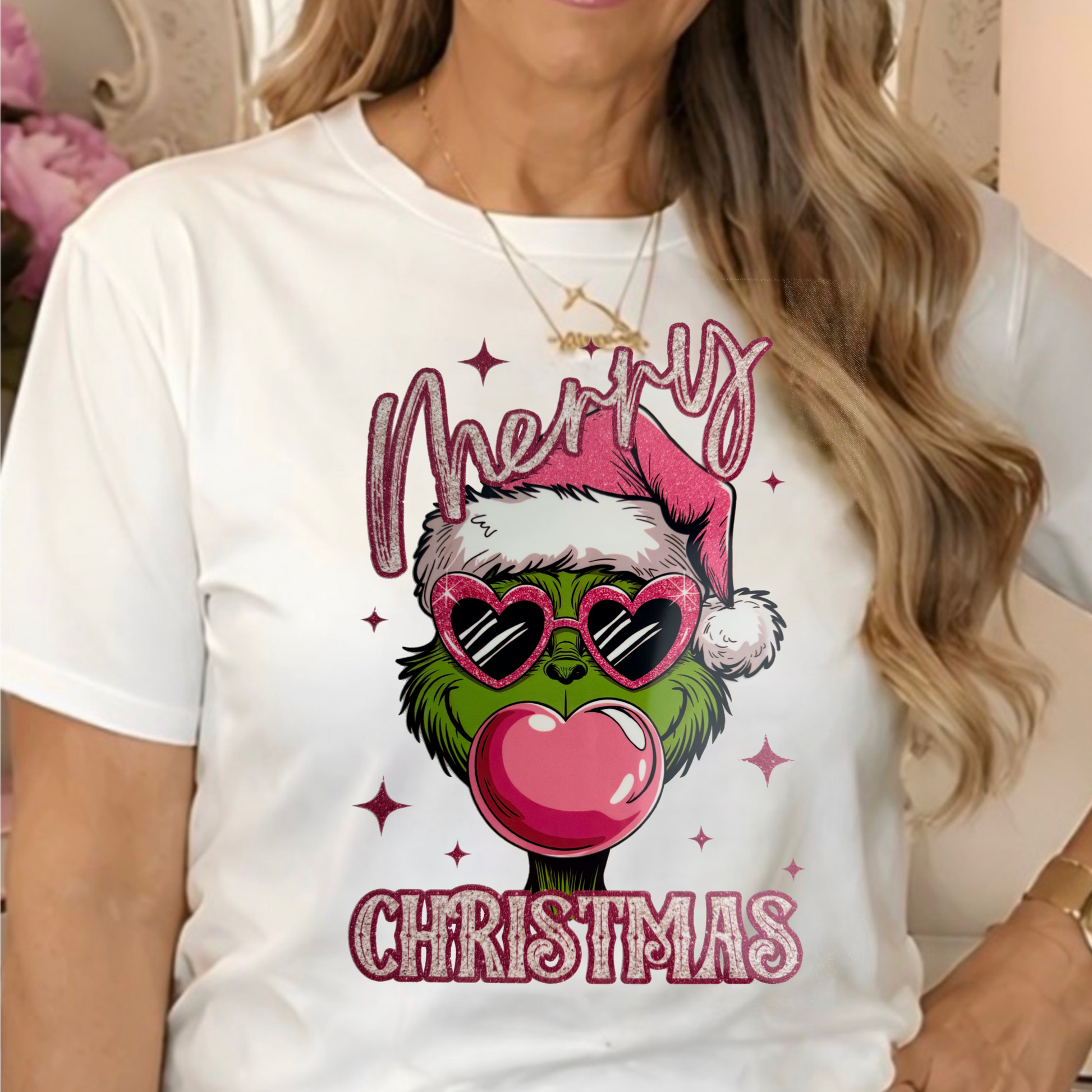 a white graphic T-shirt with a Christmas-themed Pink Bubble Grinch design and the words 'Merry Christmas".