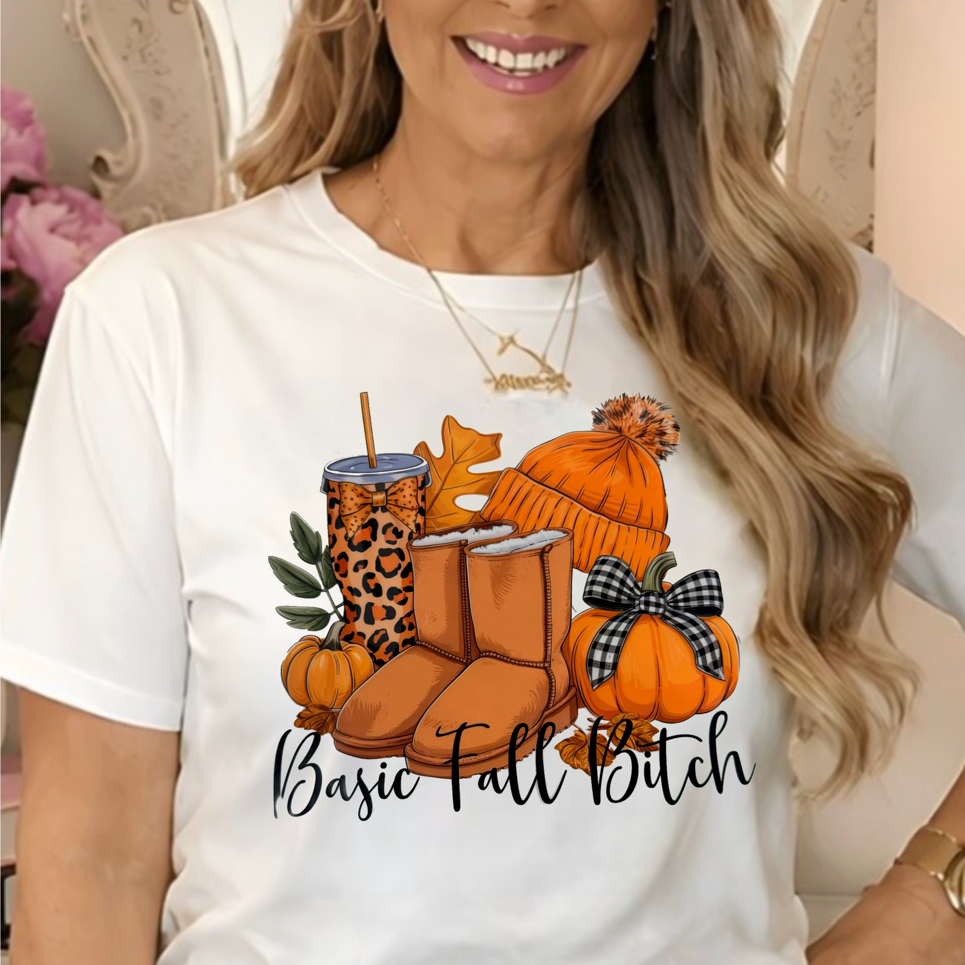 a white graphic t-shirt with a fall-themed design featuring boots, pumpkins, a hat, and the text 'Basic Fall Bitch'.