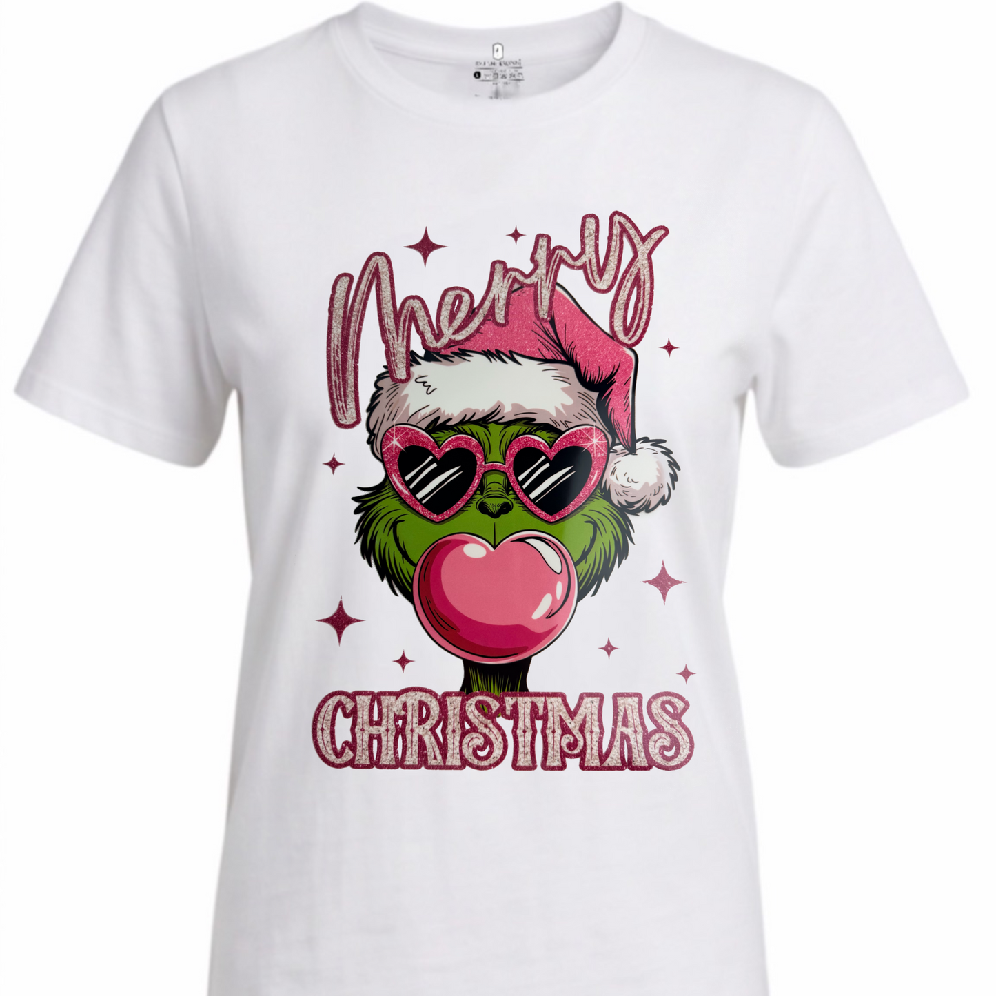 A white short-sleeve crewneck t-shirt featuring a festive graphic of the Grinch wearing a Santa hat and heart-shaped sunglasses while blowing a pink bubblegum bubble, with 'Merry Christmas' written in pink glitter-style text.