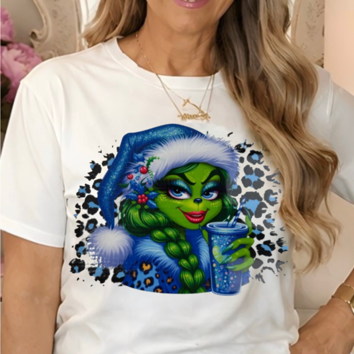 a white graphic t-shirt with a colorful print of a Grinchette in a blue Santa hat.
