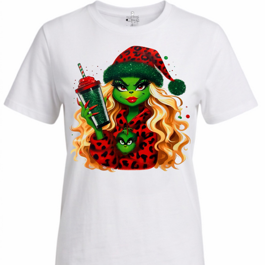 A white short-sleeve crewneck t-shirt featuring a colorful graphic print of a green-skinned woman with long wavy blonde hair, wearing a red leopard-print Santa hat and matching top, holding a green drink.